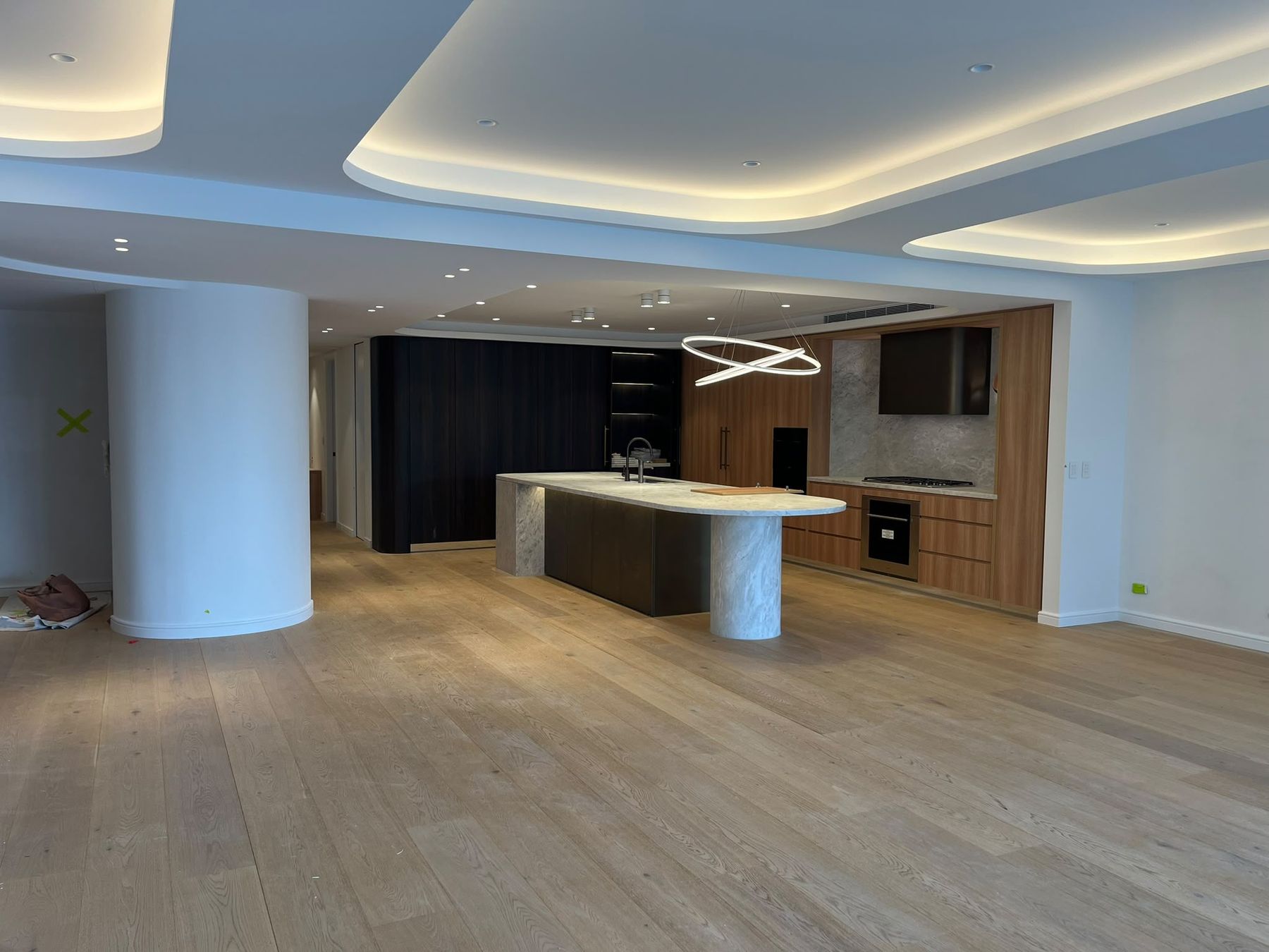 Open plan kitchen and living area with stone island bench, curved column and cove lighting