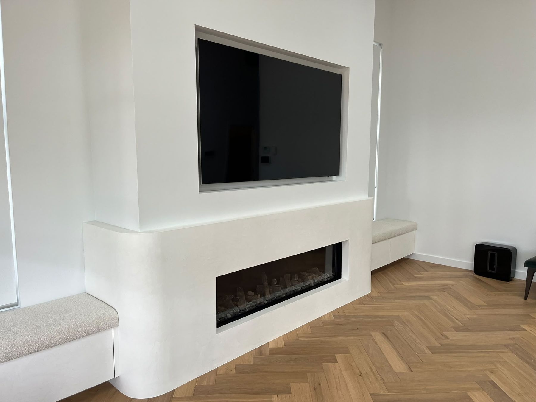 Curved microcement fireplace surround with recessed television and built-in upholstered bench seating
