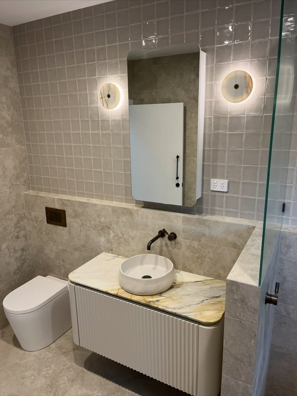 Bathroom with fluted vanity, veined marble top, round vessel basin and backlit stone disc sconces